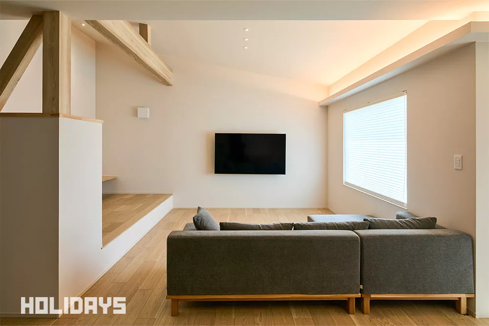 床はオーク材の突板を使用。無垢の木の質感がシンプルな空間に高級感を添えている。TVは壁面に取り付けることですっきりとした印象に。天井は間接照明やダウンライトを使用しフラットにまとめる事で、柱や梁の重厚感を引き立て、ノイズレスな中にも木の温かみを感じられるシンプルナチュラルな雰囲気を演出している。