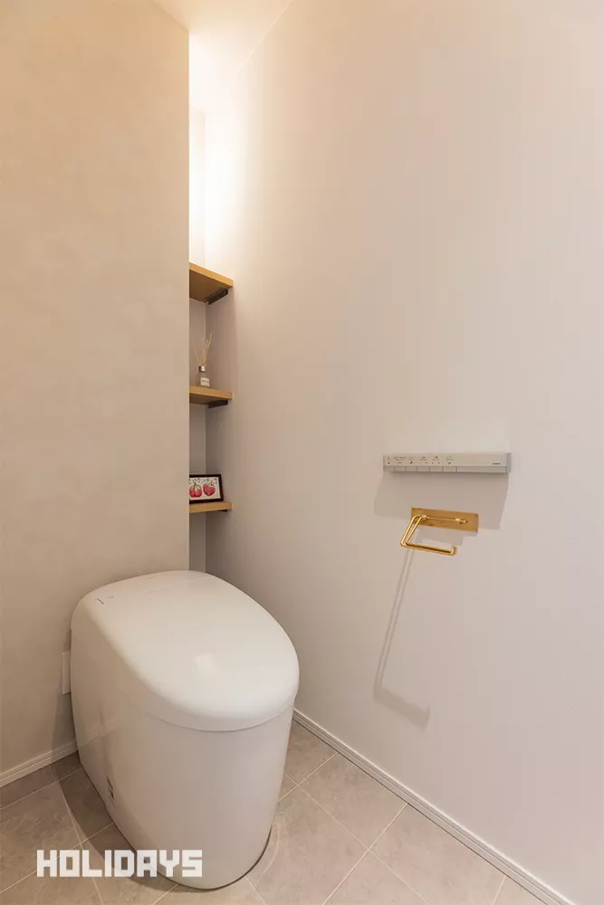 グレージュのカラーに統一したトイレには、背面の壁に見せる収納と見せない収納を兼ねた飾り棚を造作した。壁に隠れる部分にはトイレットペーパーのストックや掃除道具を隠すこともでき、実用性とデザイン性を兼ね備えている。照明器具も敢えて壁に隠す事で、間接照明の様にスタイリッシュな空間を引き立てる。